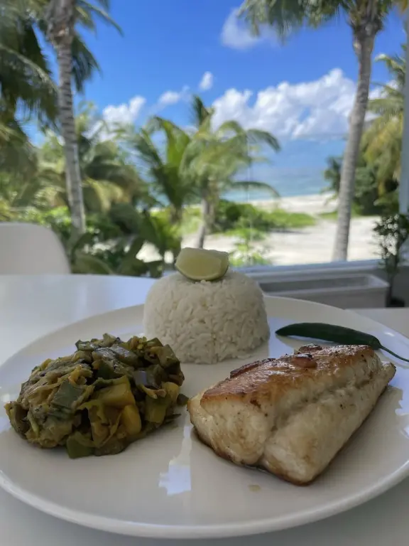 Assiette de riz, poisson et légumes servis sur une table en extérieur avec vue sur la plage.