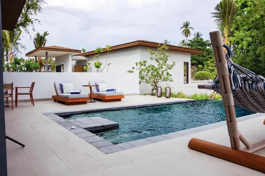 Une piscine rectangulaire avec deux transats et un hamac dans un jardin tropical.