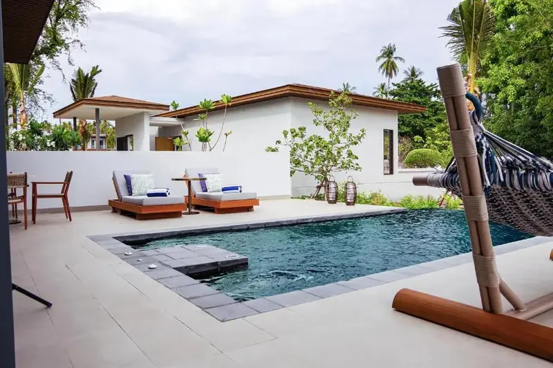 Une piscine rectangulaire avec deux transats et un hamac dans un jardin tropical.