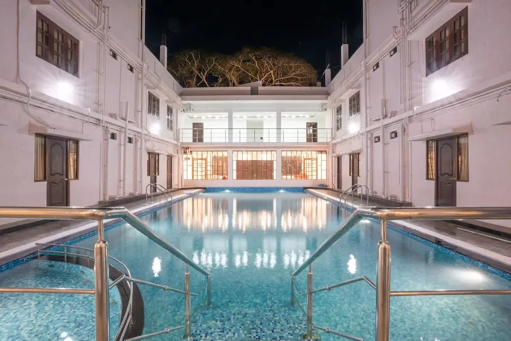 Une piscine rectangulaire illuminée au centre d'une cour intérieure.