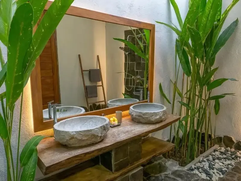 Deux vasques en pierre naturelle sur un meuble en bois, devant un grand miroir.
