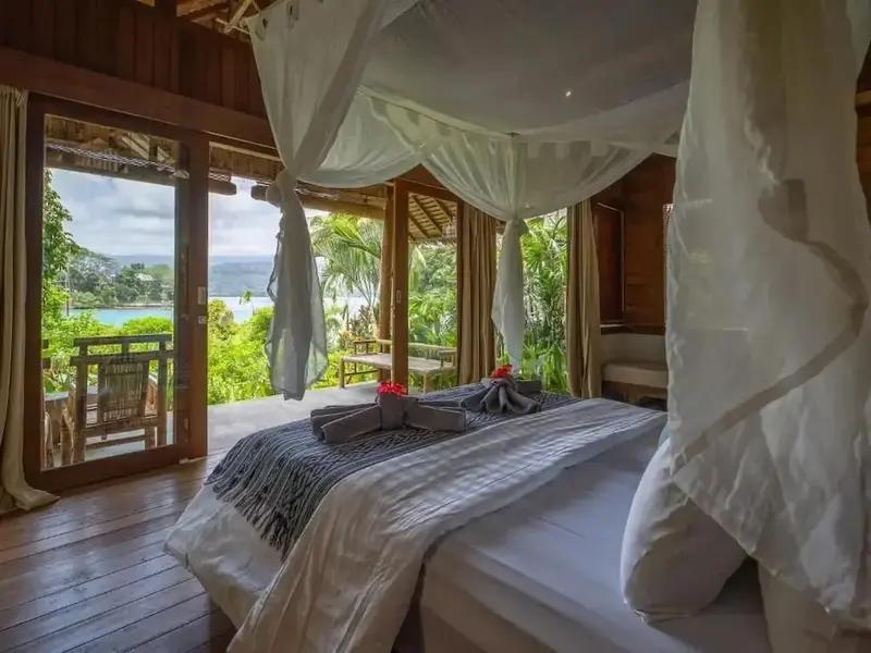 Une chambre avec un lit à baldaquin donnant sur une terrasse et une vue sur la mer.