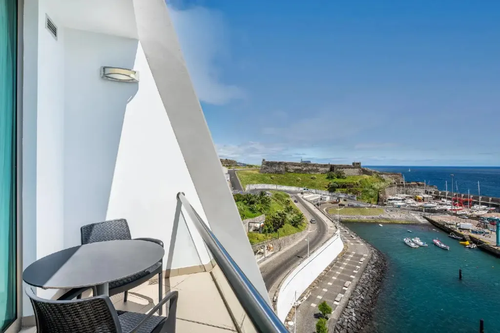 Vue d'une terrasse avec table et chaises donnant sur un port et une forteresse.
