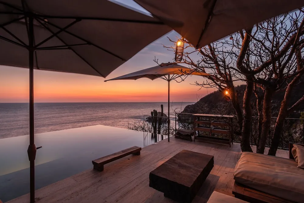 Terrasse avec piscine à débordement donnant sur la mer au coucher du soleil.