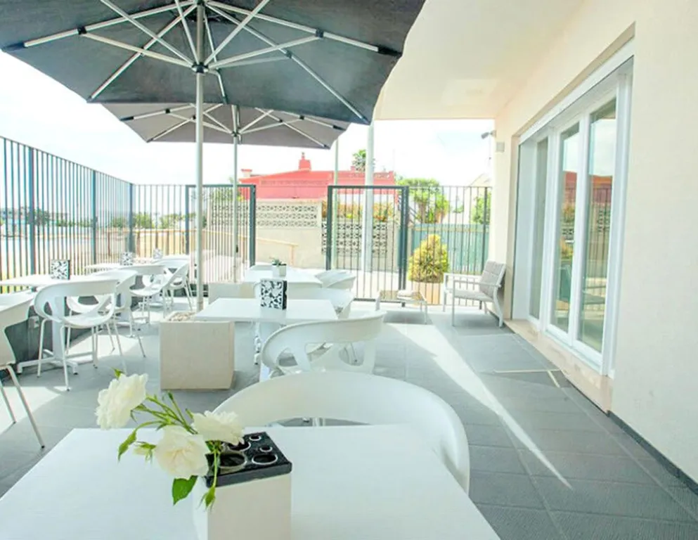 Une terrasse ombragée avec des tables et des chaises blanches offre un espace de détente extérieur.