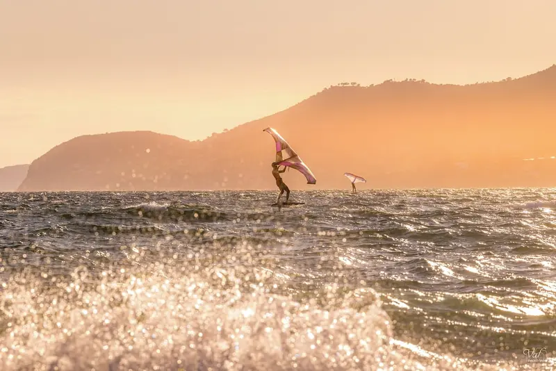 Une personne pratique la planche à voile sur une mer agitée au coucher du soleil.