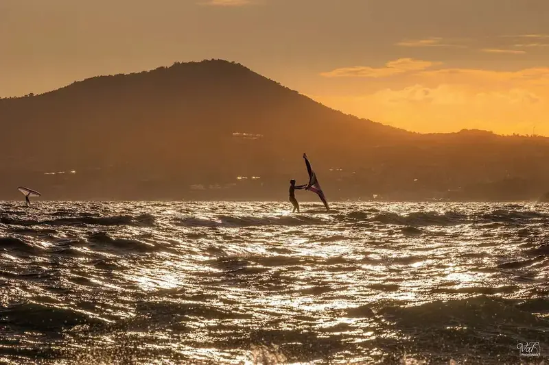 Une personne pratique la planche à voile sur une mer scintillante au coucher du soleil.