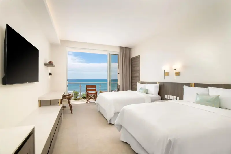 Chambre lumineuse avec vue sur la mer depuis un balcon.