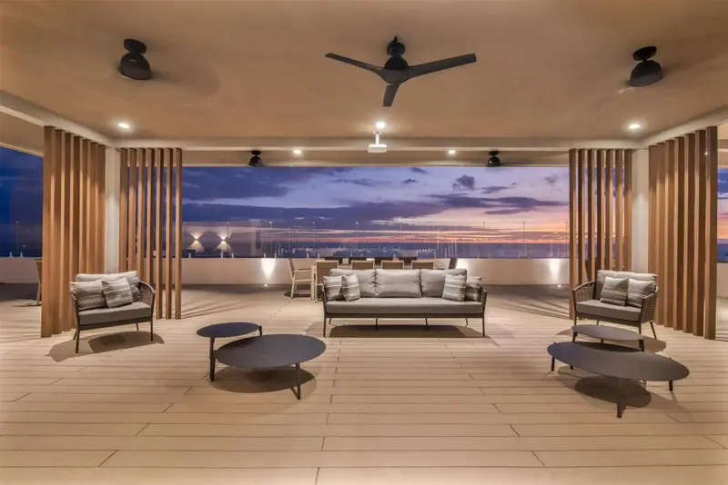 Espace de détente extérieur avec canapés et tables basses face à un coucher de soleil sur la mer.