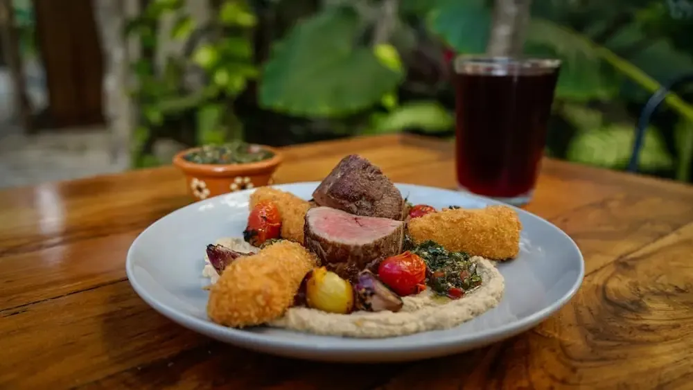 Assiette de viande accompagnée de légumes et d'une boisson sombre sur une table en bois.