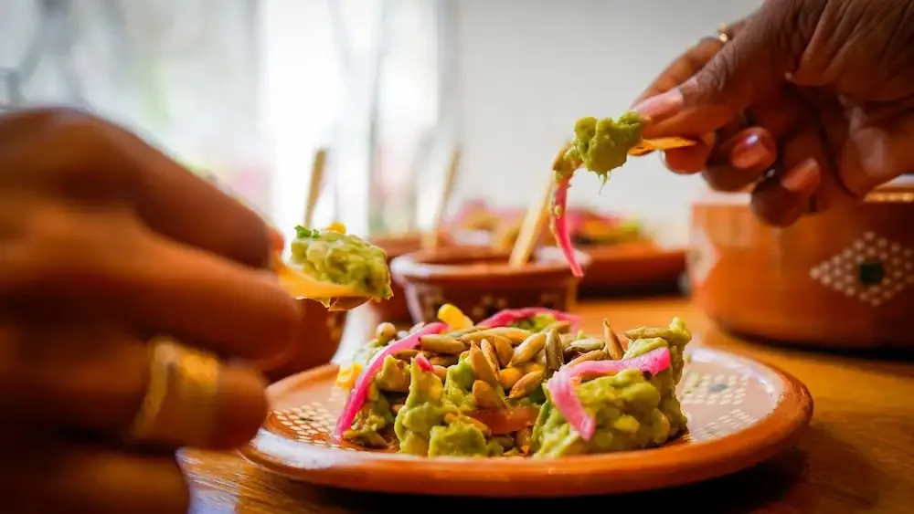 Une personne prépare une portion de guacamole sur une table en bois.