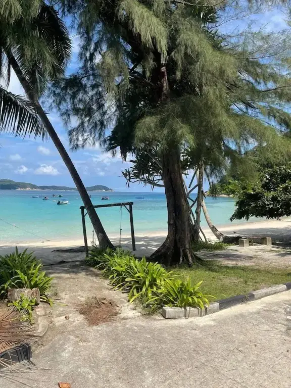 Une plage de sable blanc bordée de végétation tropicale et de bateaux amarrés dans une eau turquoise.