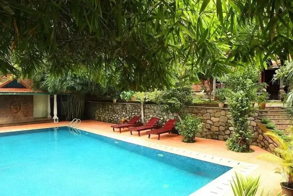 Une piscine rectangulaire bordée de transats dans un jardin luxuriant.