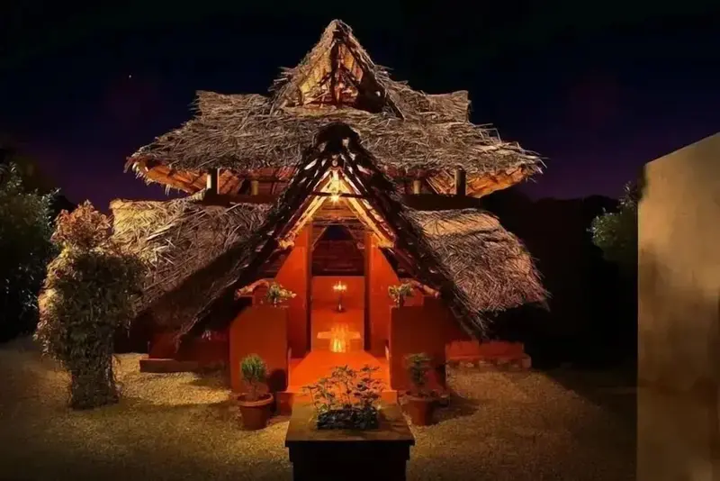 Une structure à toit de chaume illuminée la nuit.