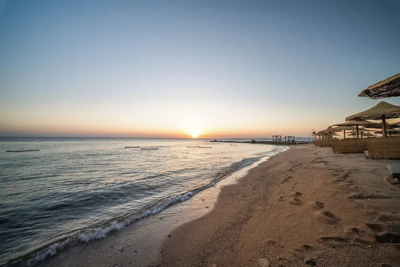 Plage de sable fin bordée par une mer calme au coucher du soleil.