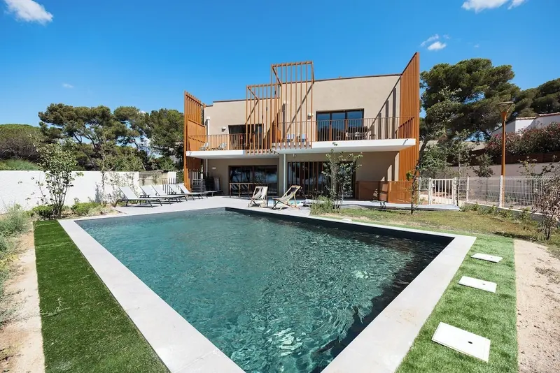 Une piscine rectangulaire se trouve devant un bâtiment moderne avec des terrasses.