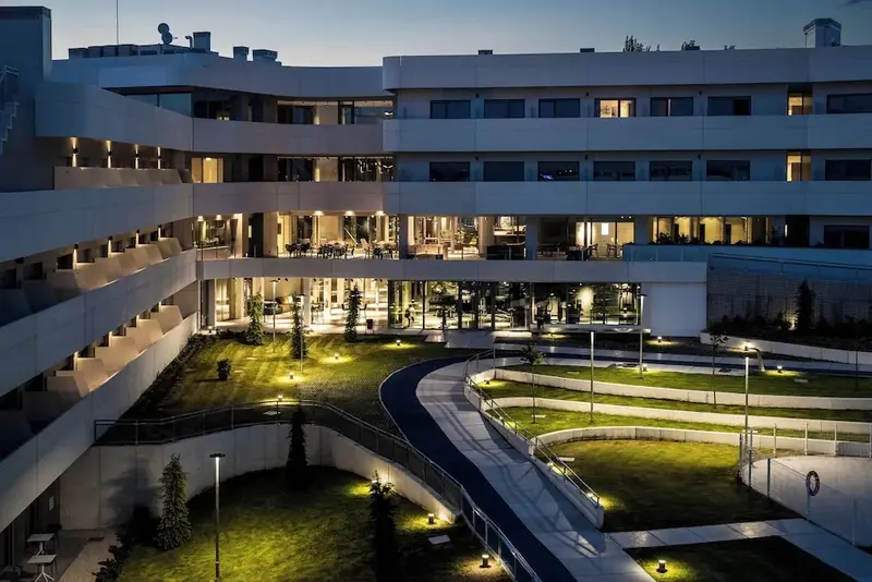 Bâtiment moderne avec des terrasses illuminées surplombant un jardin soigné.