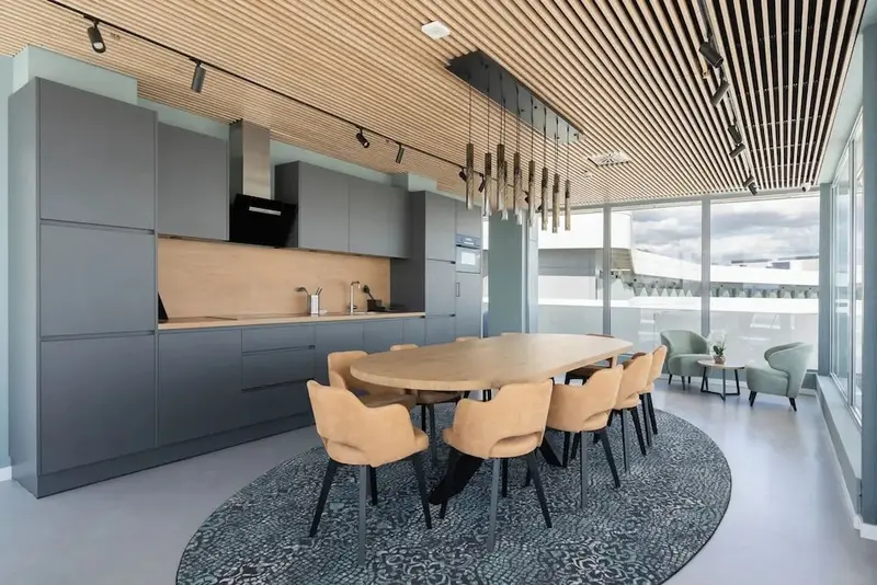 Une grande table à manger en bois est entourée de chaises dans une pièce lumineuse avec une cuisine équipée.