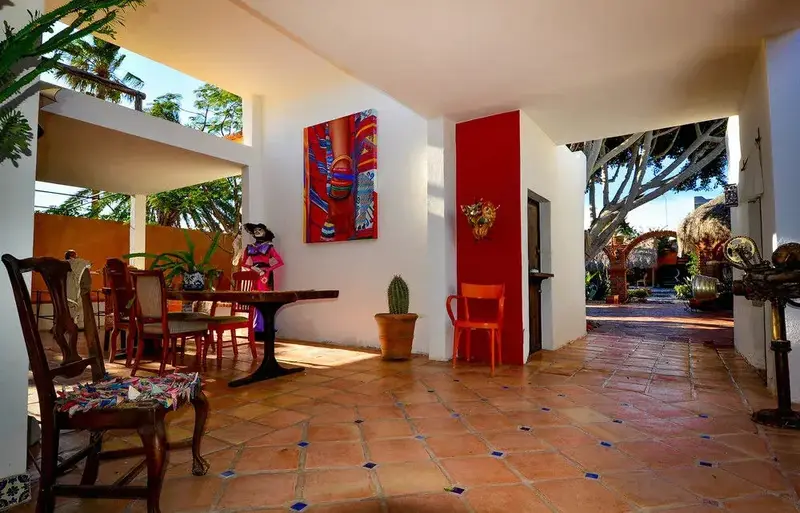Espace extérieur ombragé avec table à manger et décorations murales colorées.