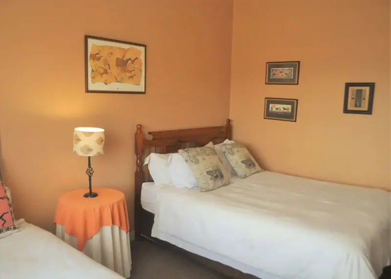 Une chambre aux murs couleur pêche avec deux lits simples et des tableaux décoratifs.