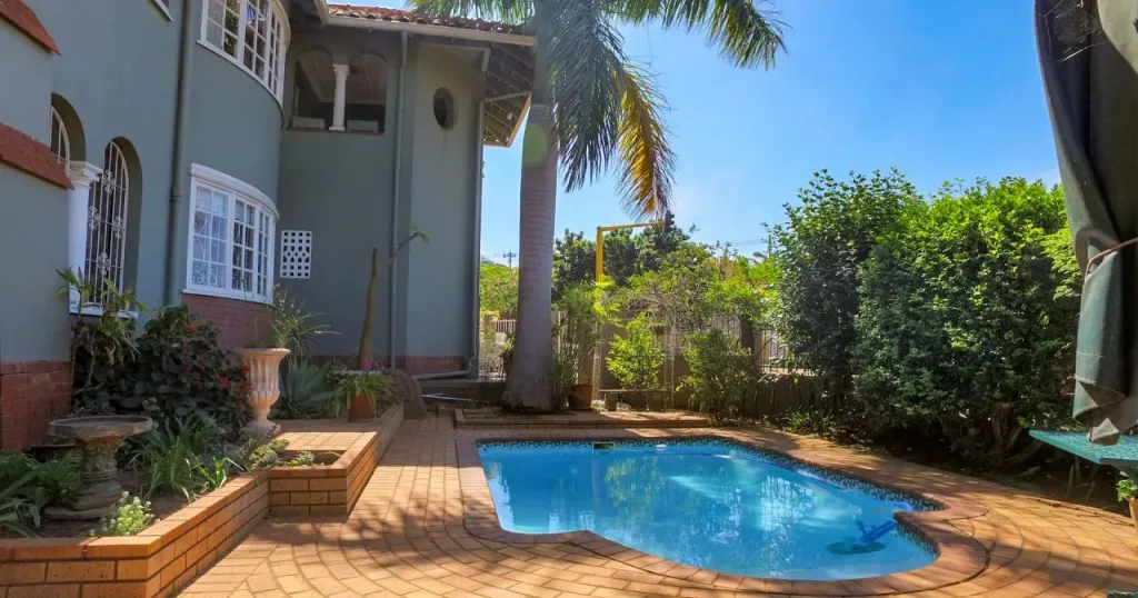 Une piscine rectangulaire est entourée d'une terrasse pavée et de végétation luxuriante.