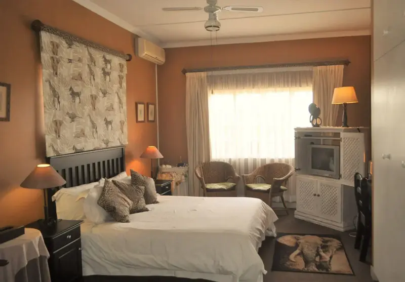 Une chambre à coucher lumineuse avec un grand lit et deux fauteuils près d'une fenêtre.