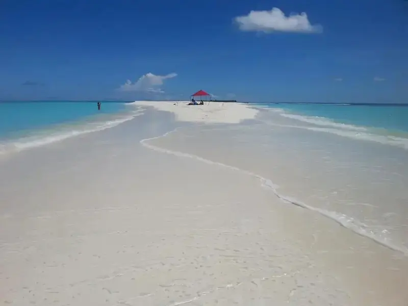 Vaste plage de sable blanc bordée d'eau turquoise sous un ciel bleu nuageux.
