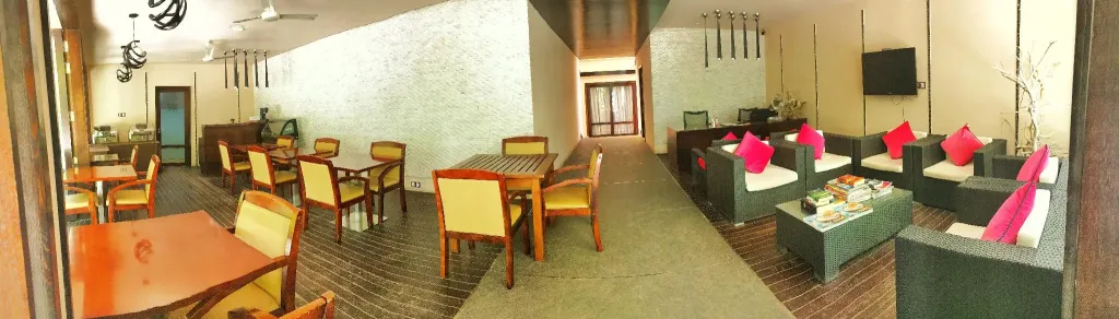 Une salle lumineuse avec des tables et des chaises disposées pour les repas, ainsi qu'un coin salon avec des canapés et des coussins.