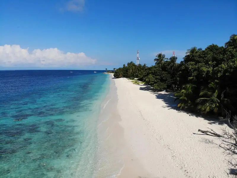 Plage de sable blanc bordée d'une eau turquoise et d'une végétation luxuriante.