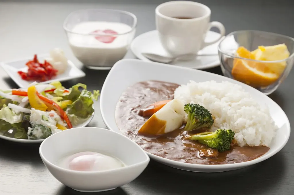 Assiette de curry japonais avec riz, accompagnée de salade, de fruits et d'une boisson.