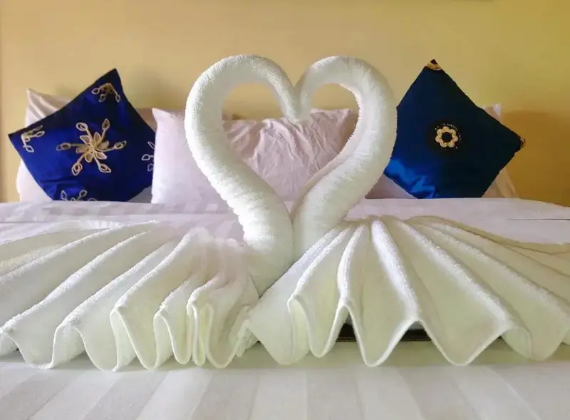 Un lit est orné de serviettes pliées en forme de cygnes et de cœur.