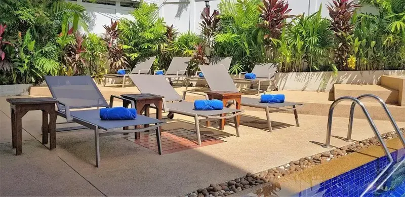 Transats bleus disposés autour d'une piscine ensoleillée, avec une végétation luxuriante en arrière-plan.