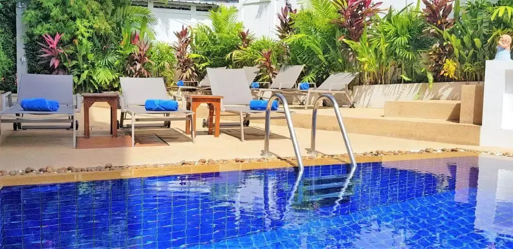 Transats bleus alignés au bord d'une piscine ensoleillée, entourée d'une végétation luxuriante.