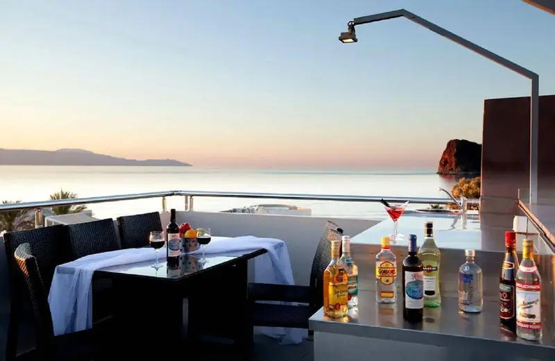 Terrasse avec table et bar offrant une vue sur la mer au coucher du soleil.