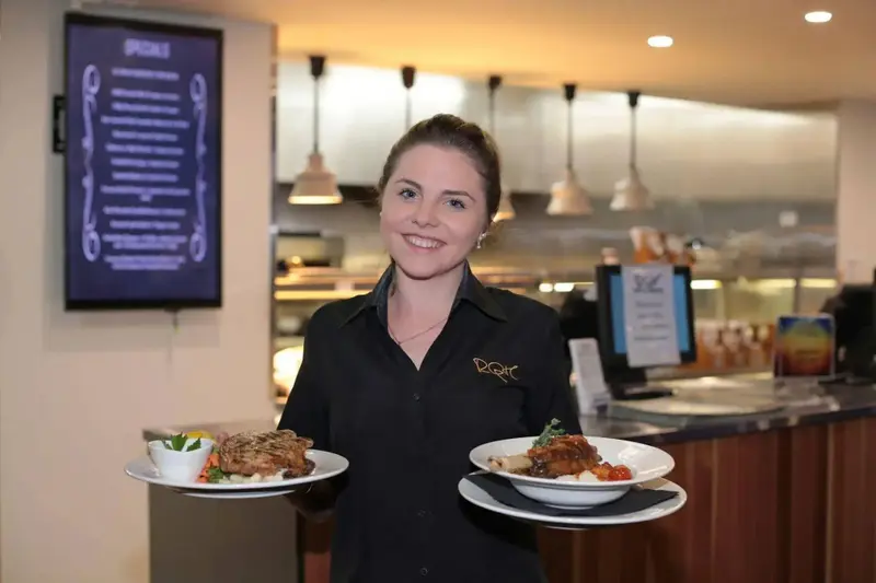 Une serveuse souriante présente deux plats préparés dans un espace lumineux.