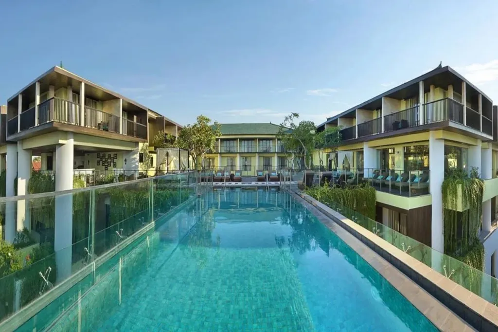 Une piscine rectangulaire bordée de transats et de bâtiments à balcons.
