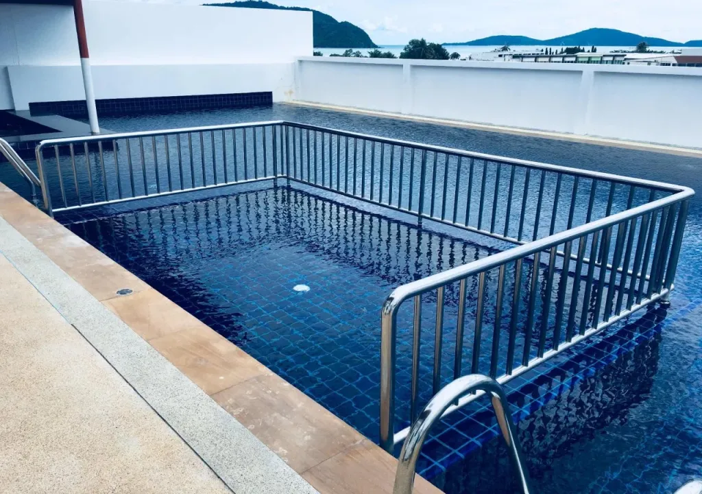Une piscine rectangulaire entourée d'une rambarde métallique, avec une vue sur la mer et les îles au loin.