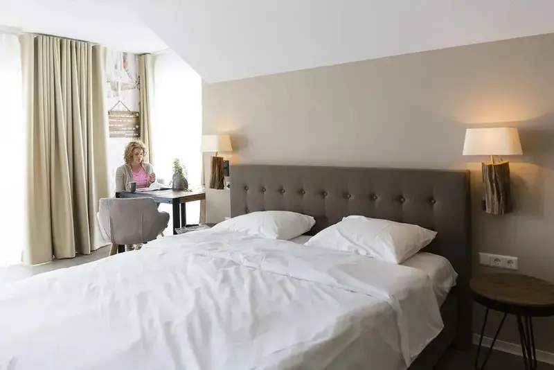 Une chambre lumineuse avec un lit double et un bureau près de la fenêtre.