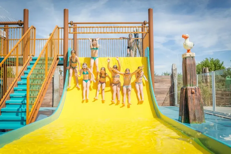 Des enfants glissent sur un toboggan aquatique jaune dans une zone de jeux.