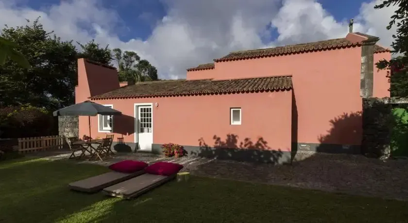 Bâtiment rose avec terrasse et pelouse verdoyante sous un ciel nuageux.