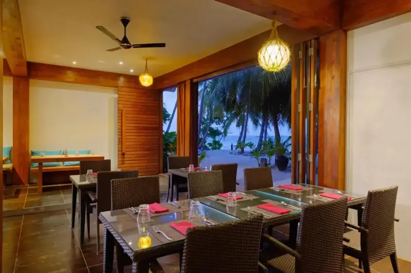 Une salle à manger lumineuse s'ouvre sur une plage de sable fin bordée de palmiers.