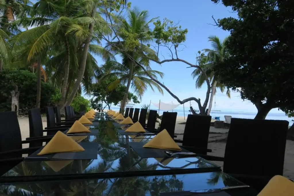 Tables dressées en extérieur face à la mer et aux palmiers.