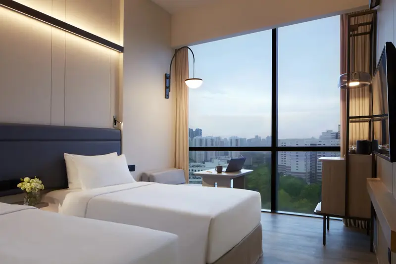 Chambre lumineuse avec deux lits simples et vue sur la ville.