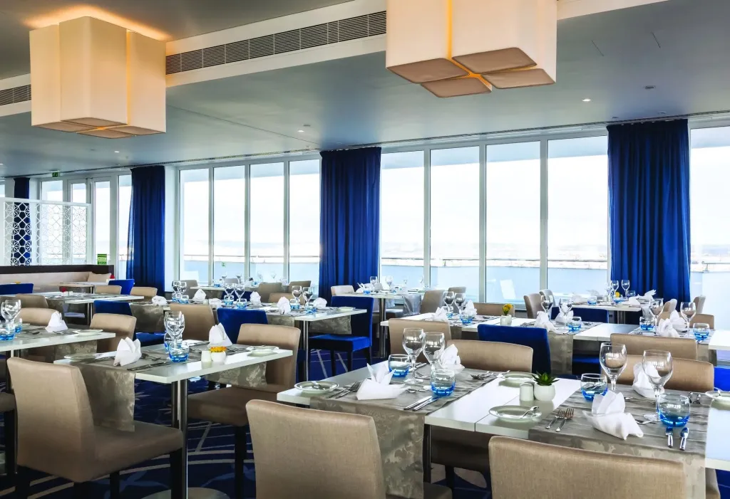 Une salle lumineuse avec des tables dressées face à une vue sur la mer.