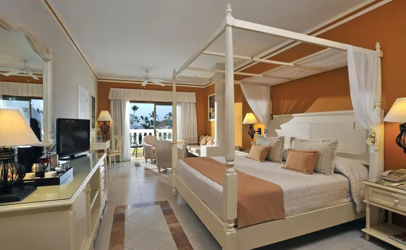 Une chambre lumineuse avec un grand lit à baldaquin et un accès à un balcon.