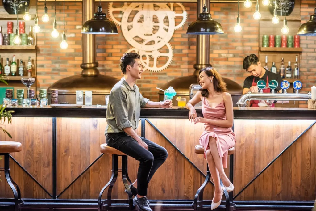 Un couple est assis au comptoir d'un bar, des boissons colorées devant eux.