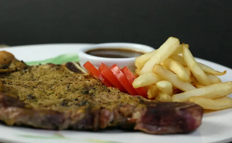 Une portion de viande grillée accompagnée de frites et d'une sauce.