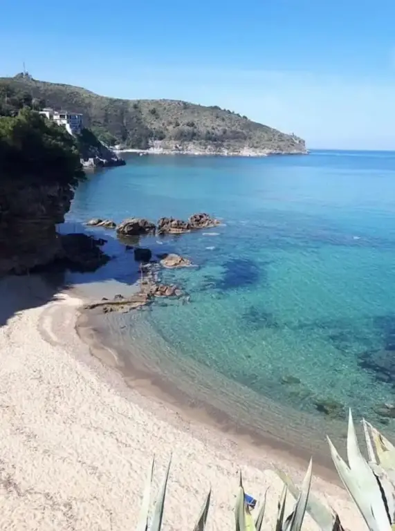 Une plage de sable fin bordée d'une eau turquoise et de rochers.