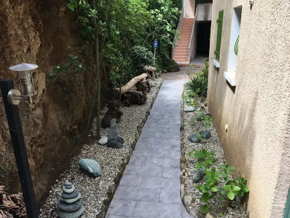 Un chemin pavé traverse un jardin étroit et ombragé.