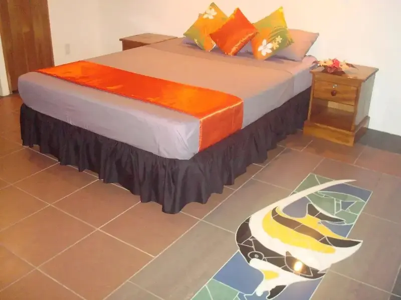 Une chambre lumineuse avec un lit recouvert d'une courtepointe orange et de coussins colorés.